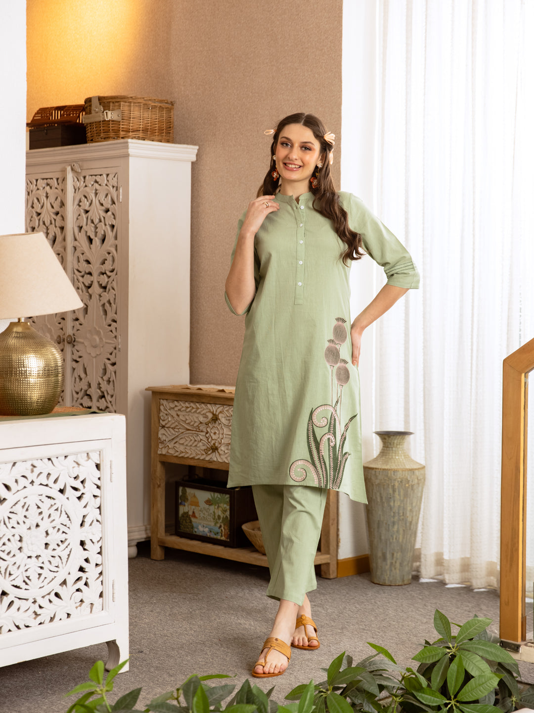 A model wearing a sage green pure cotton kurta set with elegant floral embroidery work by Aadews Jaipur, featuring 3/4 sleeves, mandarin collar, and matching straight pants.